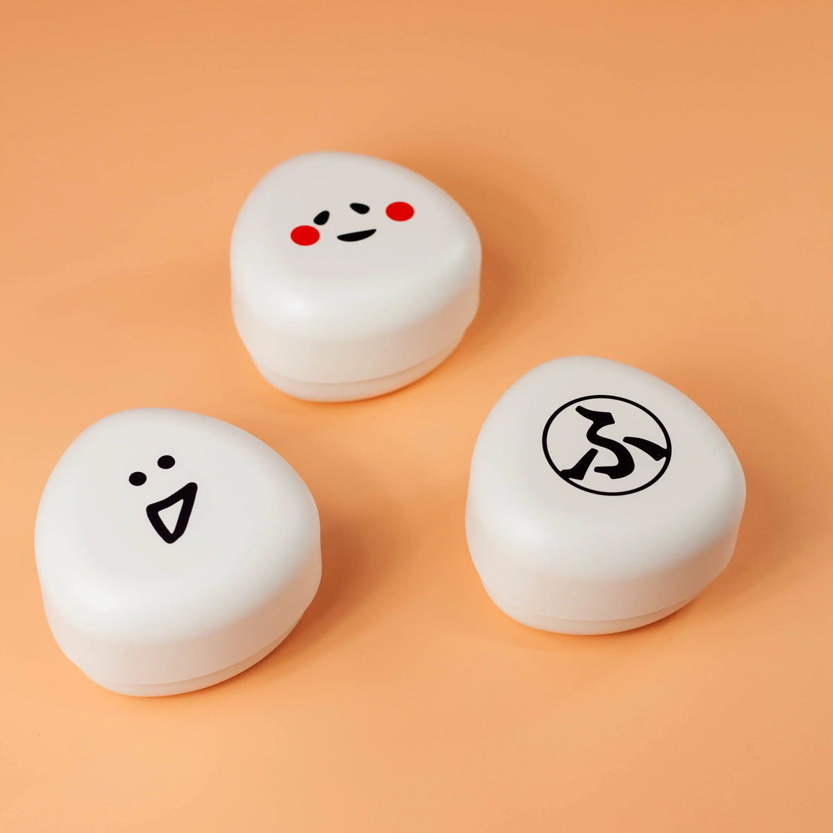オレンジの背景に並べたfufufuおにぎりケース3柄 ふ、かお、おこめ