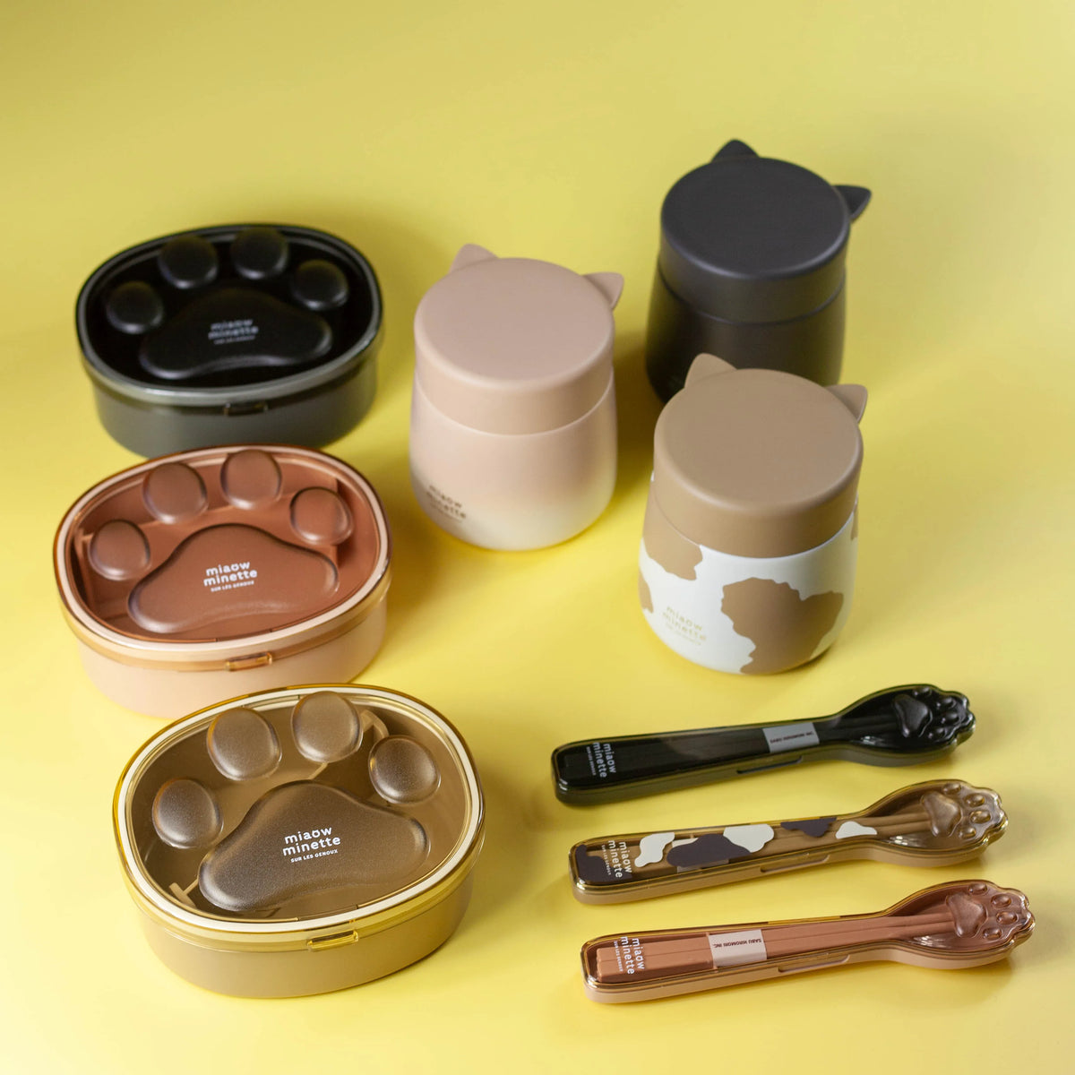 黄色の背景に並べたにゃおシリーズのねこみみポット、肉球弁当箱、箸とスプーンのコンビセット
