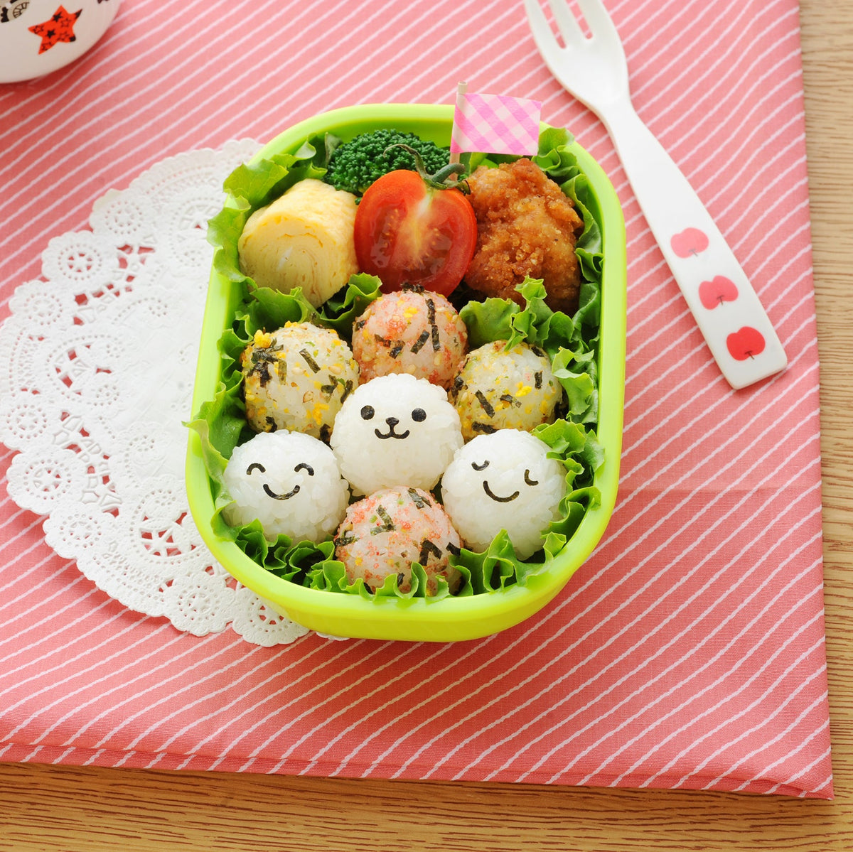 こむすびボール miniで作った笑顔おにぎり入りお弁当 — ピンクのランチョンマットとフォークを添えたテーブルコーデ