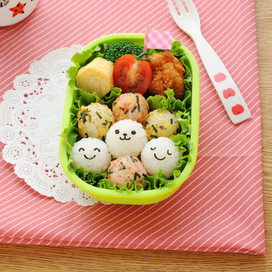 こむすびボール miniで作った笑顔おにぎり入りお弁当 — ピンクのランチョンマットとフォークを添えたテーブルコーデ